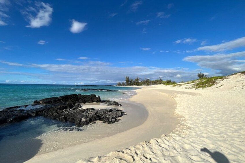 Ein Strand mit weißem Sand, einer felsigen Küstenlinie und klarem, blauem Wasser. 1