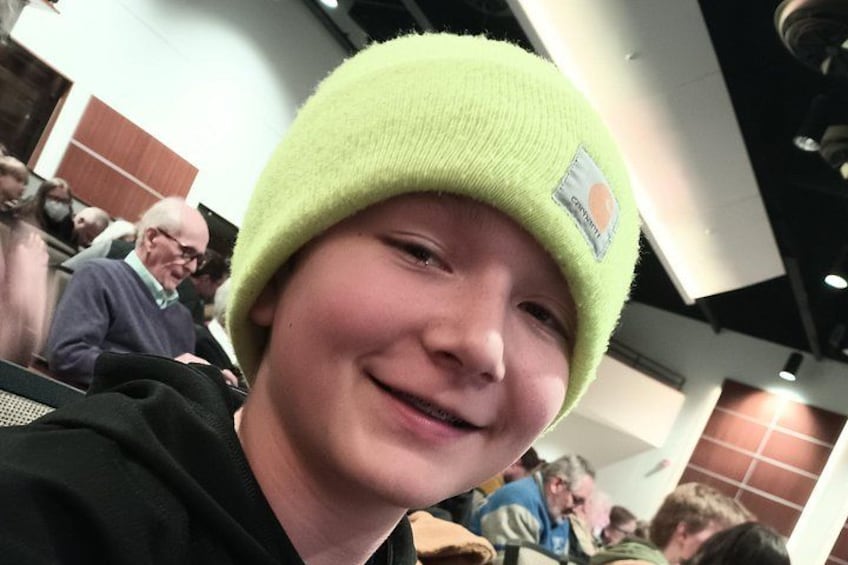 A person wearing a bright green beanie in an indoor setting with other people around. 3