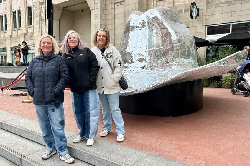Three people standing in front of a large, metallic sculpture. 2