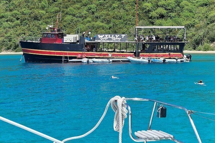 A large boat named 'WILLY T' docked at a pier with clear blue water and a forested shoreline in the background. 3