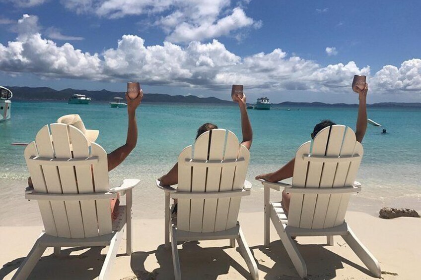 Three people sitting on beach chairs facing the ocean, with their arms raised. 2