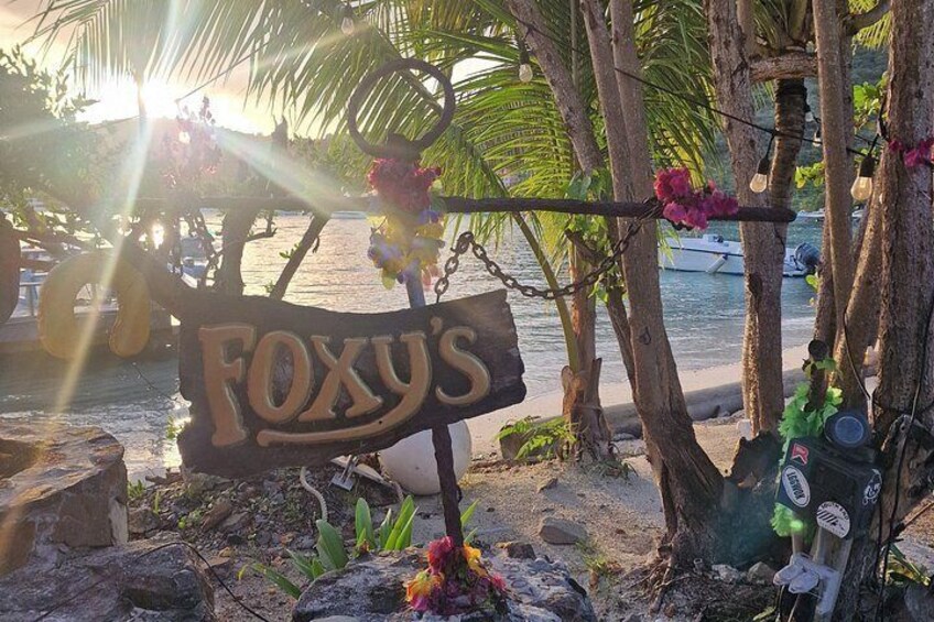A wooden sign with the name 'FOXY'S' in a tropical setting with palm trees and a beach in the background. 4