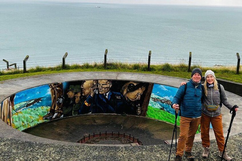 A circular mural with a coastal scene, a person standing with a walking stick, and a body of water in the background. 2