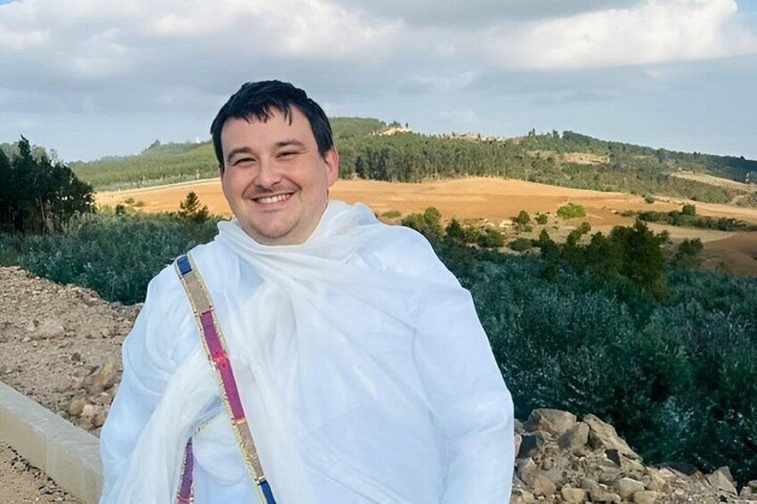 Una persona vestida de blanco de pie en un paisaje rural con colinas onduladas y vegetación escasa. 3