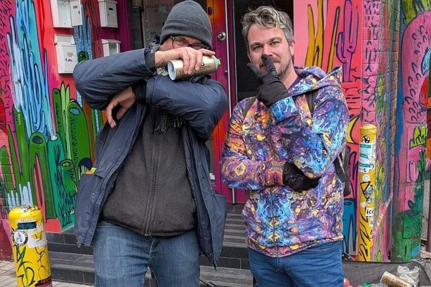 Two people standing in front of a colorful graffiti wall. 5