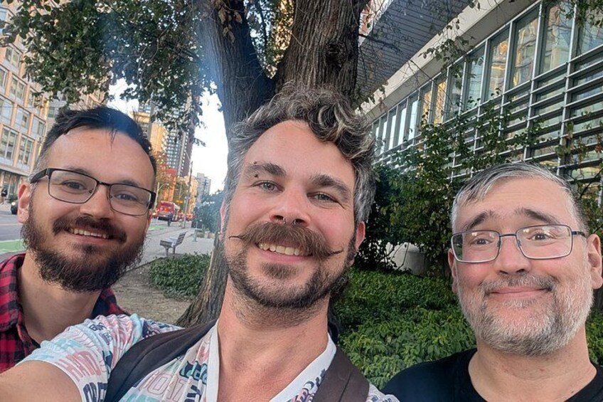 Three people taking a selfie in an urban setting with buildings and trees in the background. 2