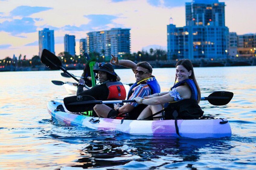 Three people kayaking on a body of water with a city skyline in the background. 5