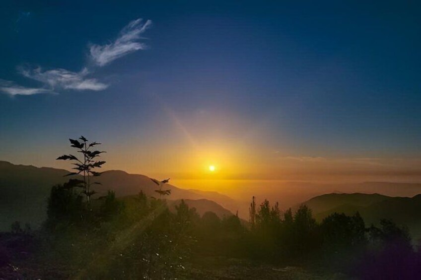 A sunrise over a mountainous landscape with silhouettes of trees and a clear sky. 1