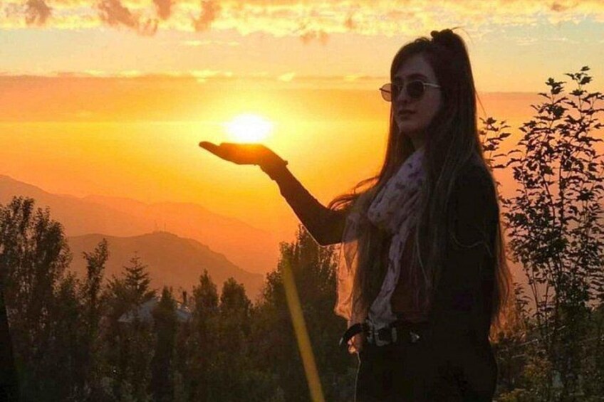 A person standing with a hand raised, sun visible in the background, and mountains in the distance. 5