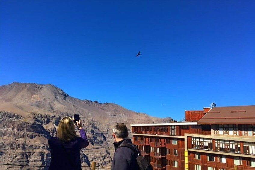 A mountainous landscape with a clear sky, a building with a red roof, and a person taking a photo. 3
