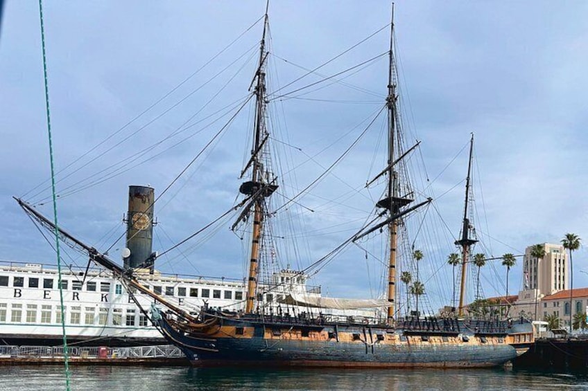 A large sailing ship docked at a harbor with a modern building in the background. 3