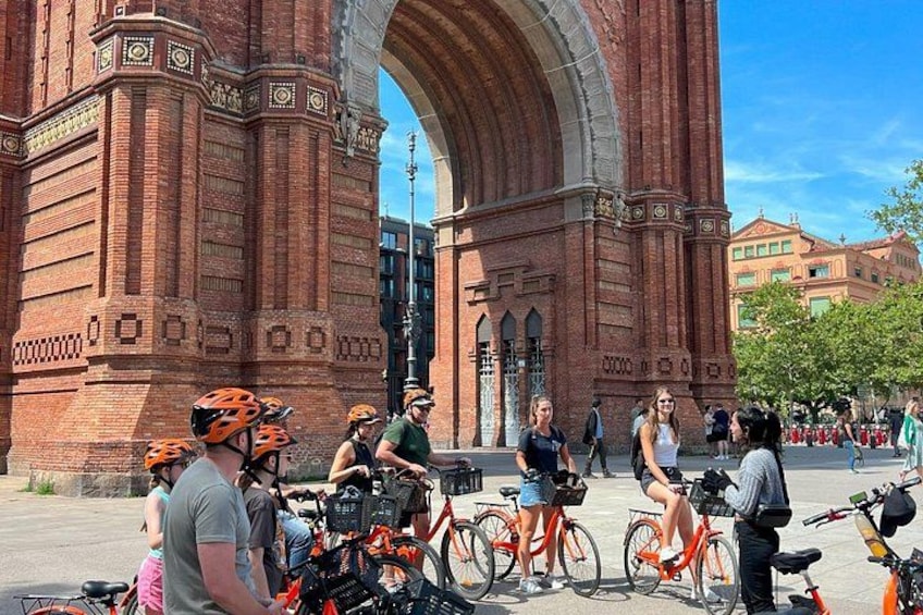 A group of cyclists in front of a large brick archway with a clear sky in the background. 4
