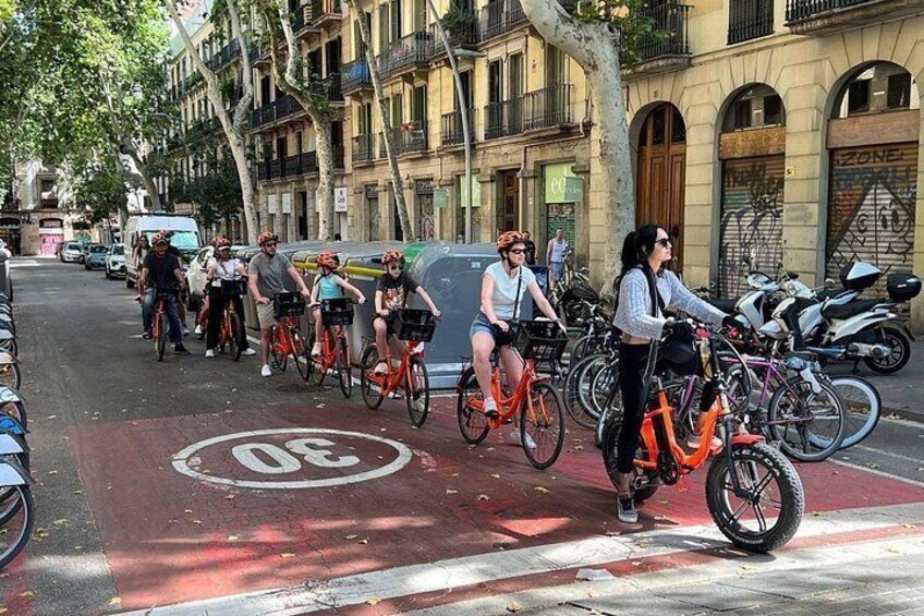 A group of cyclists on a city street with parked motorcycles and buildings in the background. 2