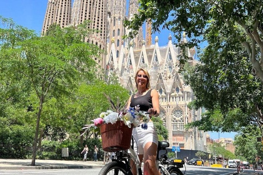A person on a bicycle with a basket, trees, and a large building in the background. 5