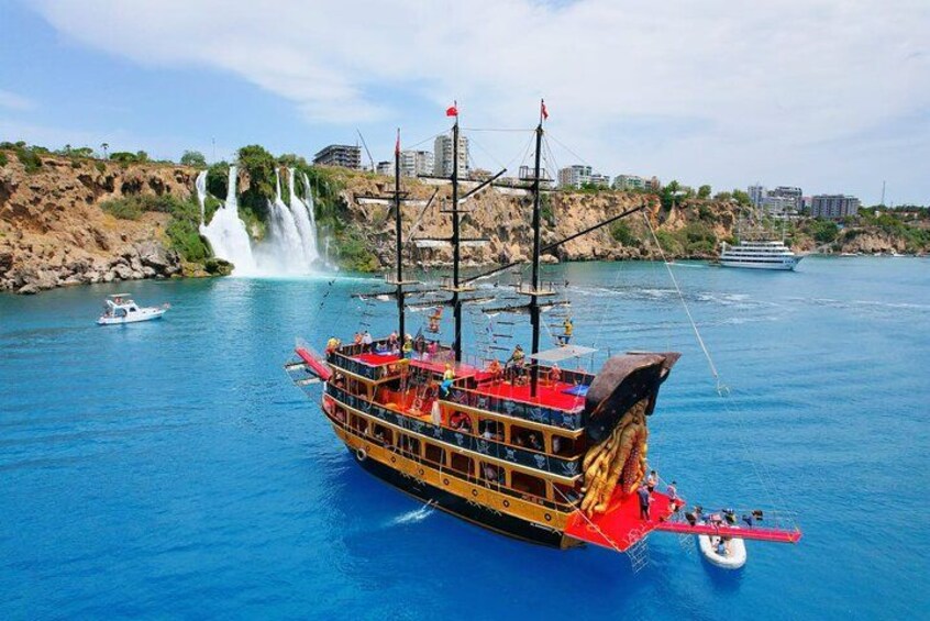 Ein großes, mehrstöckiges Boot mit rotem und goldenem Dekor, ein Wasserfall im Hintergrund und eine felsige Küstenlinie. 1