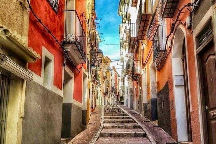 Une rue étroite, avec des bâtiments peints en rouge et en blanc, un escalier qui monte et un ciel d’un bleu limpide. 1