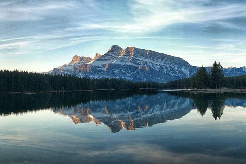 Une chaîne de montagnes se reflète dans un lac paisible, avec une forêt au premier plan. 3