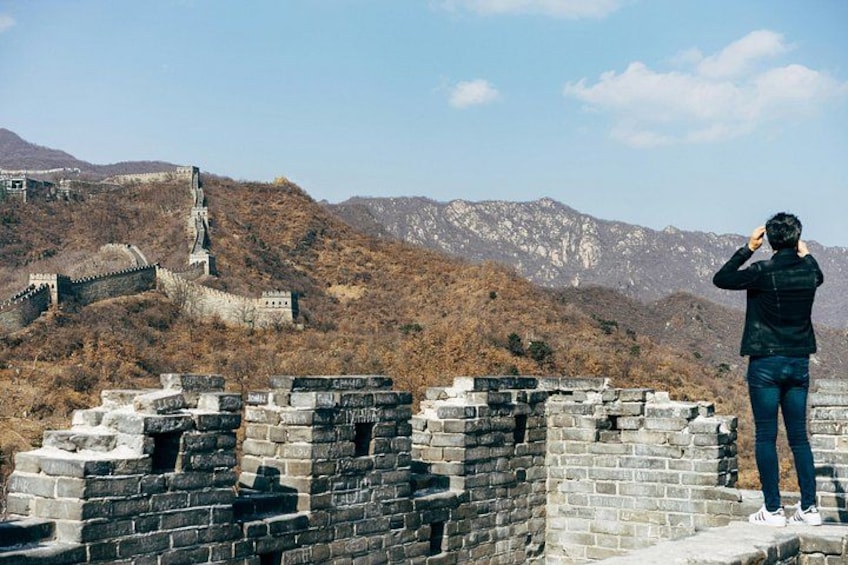 A person standing on the Great Wall of China, overlooking the wall and the surrounding mountainous landscape. 4