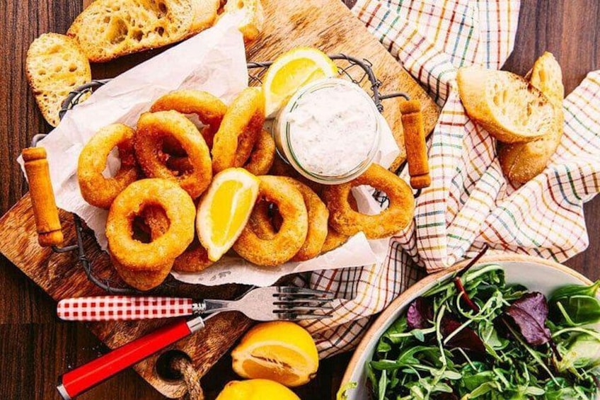 A wooden board with fried onion rings, lemon wedges, and a bowl of salad. 2