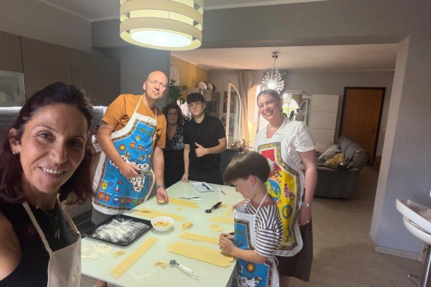 A group of people in a kitchen, some wearing aprons, with a table covered in food items and utensils. 4