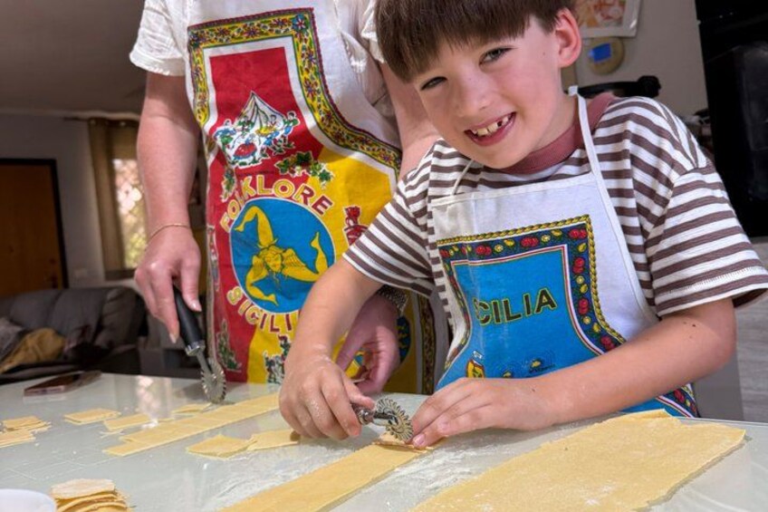 Two people wearing aprons, one cutting dough on a table. 3