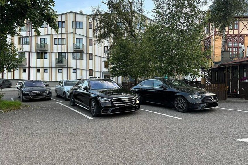 Een parkeerplaats met auto's, een meerlaags gebouw met balkons en bomen. 2