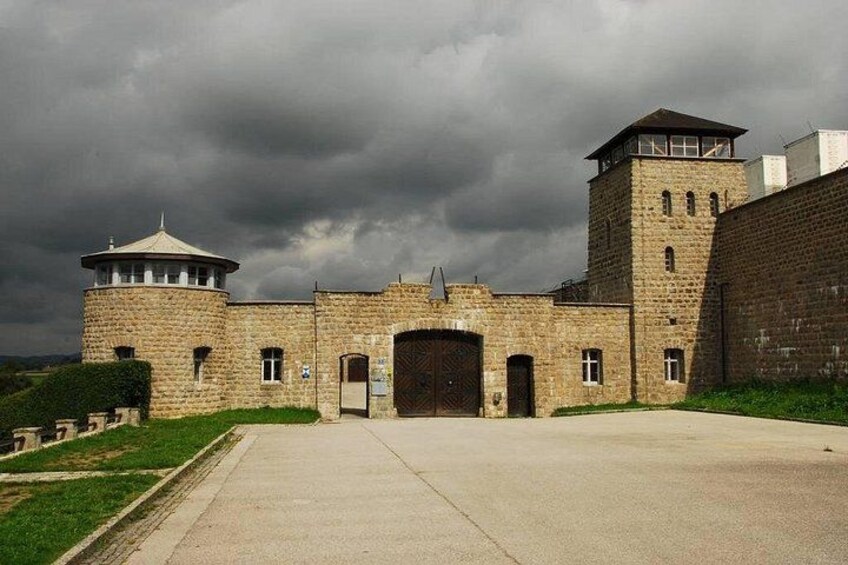 A large stone building with a central entrance, a watchtower, and a brick wall. 2