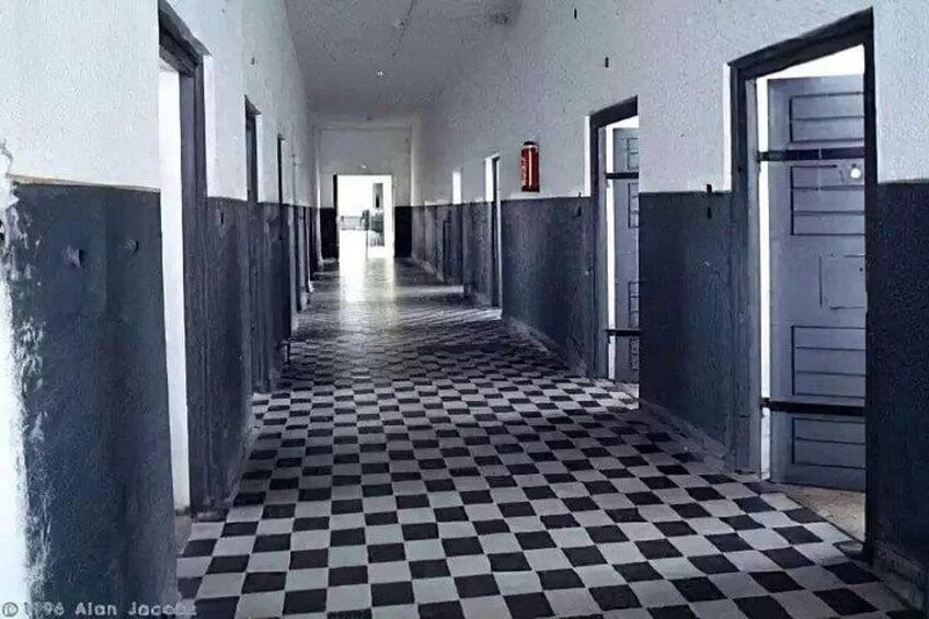 A long corridor with checkered flooring, doors on both sides, and a fire extinguisher on the wall. 2