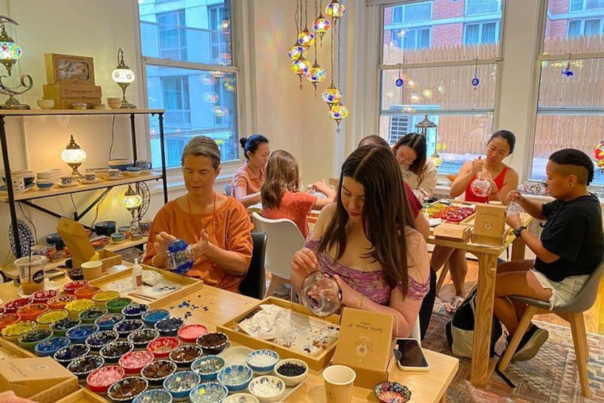 A group of people engaged in a craft activity, with bowls of colored materials and tools on a table. 2