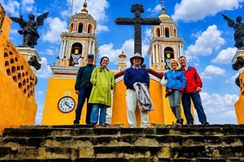 A group of people standing on steps with a clock and two bell towers in the background. 1