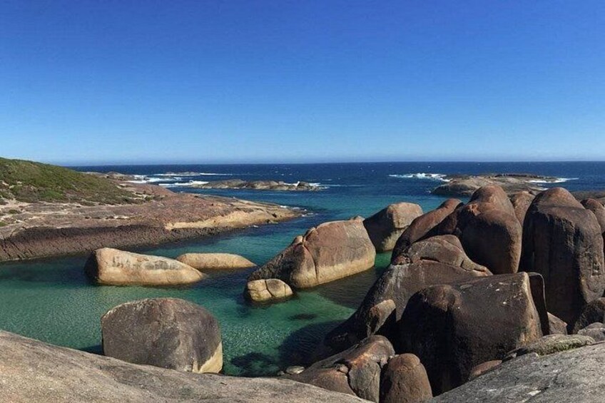 A coastal landscape with large boulders and clear turquoise water. 3