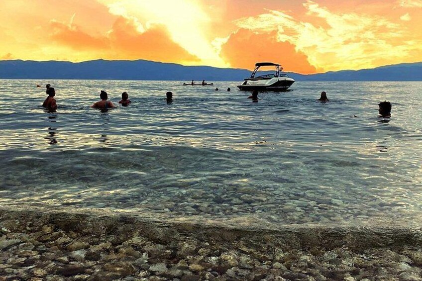 A sunset over a body of water with people swimming and a boat. 3