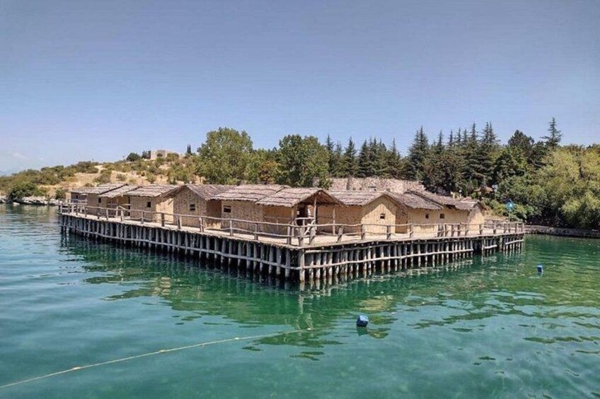 A floating house on stilts in a body of water, surrounded by trees and a distant hill. 2