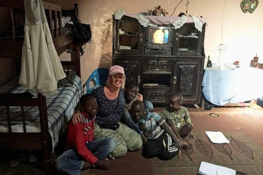 A woman sitting on the floor with four children in a room with a television and a table. 4
