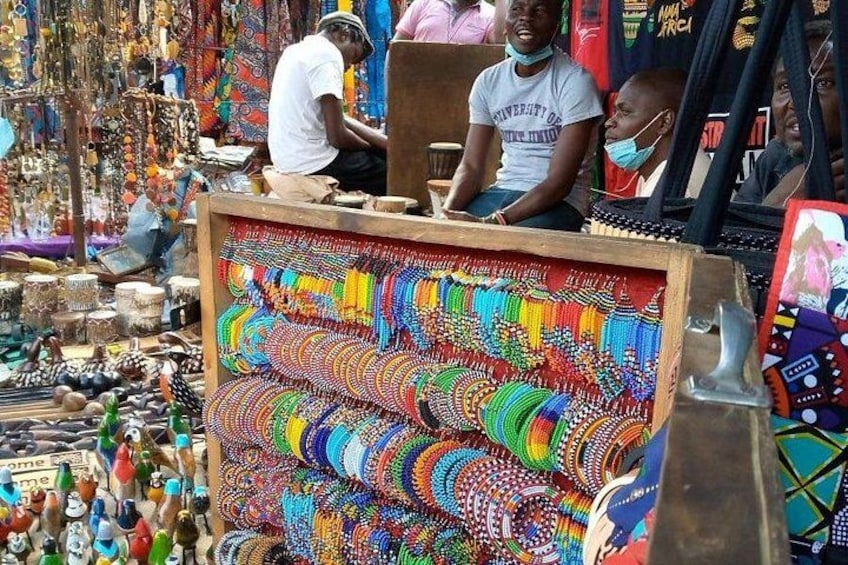 A market stall with colorful beaded jewelry and a man working on a wooden frame. 5