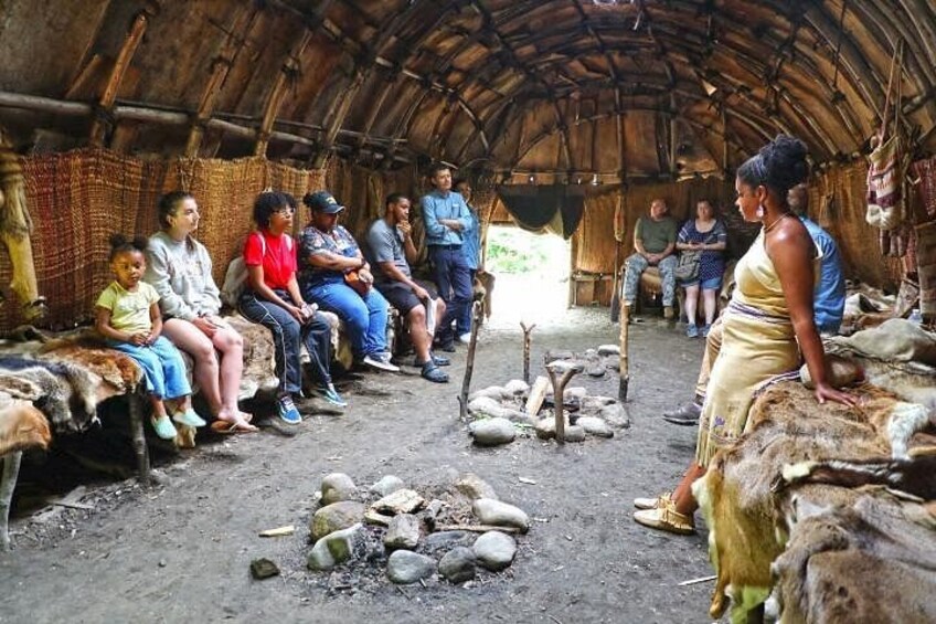 A group of people sitting on benches inside a hut with a thatched roof. 1