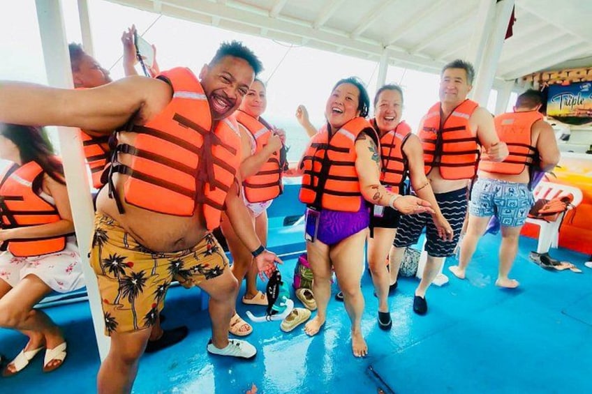 People on a boat wearing life jackets, some in swimwear, with a blue floor and a tropical-themed environment. 2