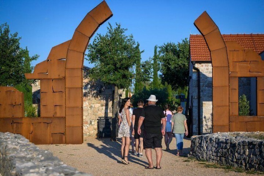 A pathway leading through a rustic gate with stone walls and a clear blue sky. 1