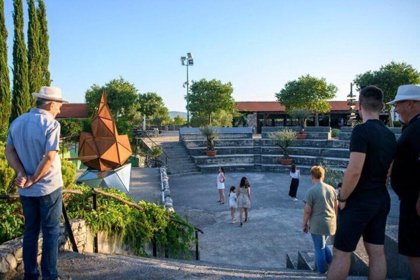 A public square with a geometric sculpture, steps leading to a building, and people walking. 3