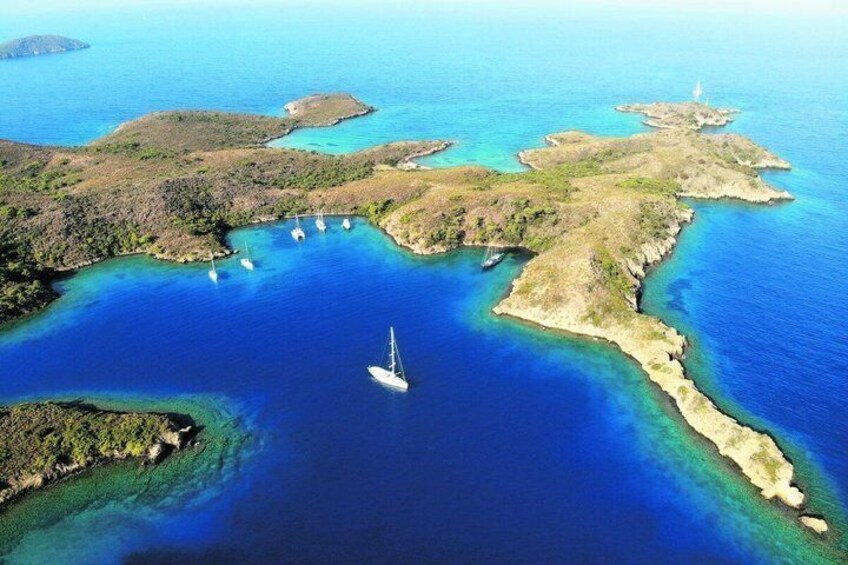 An aerial view of a coastal area with clear blue waters, several small islands, and a sailboat in the center. 3