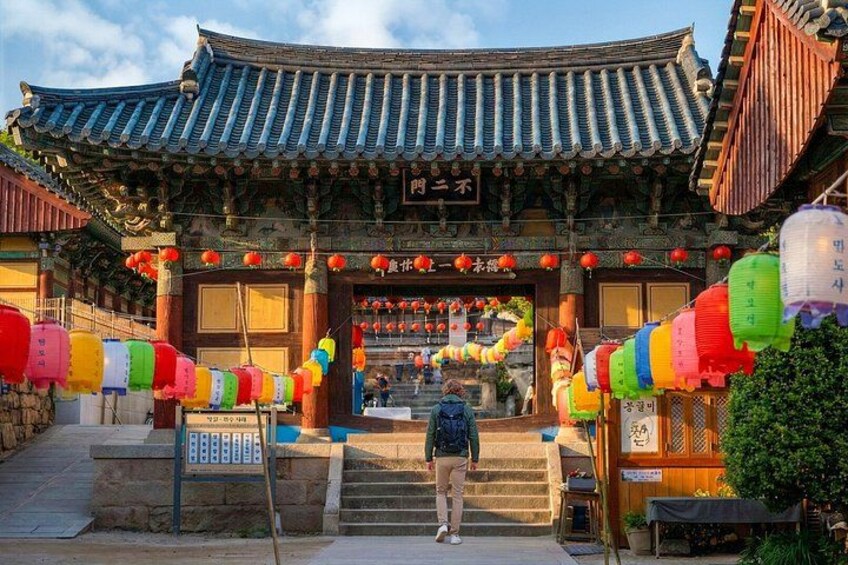 A traditional Korean gate with colorful lanterns and a person walking up the steps. 4