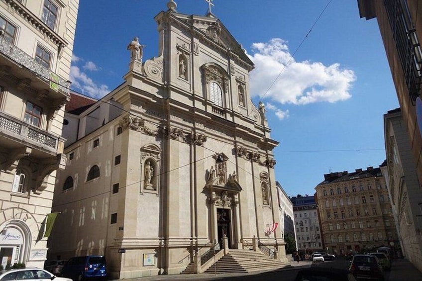 En historisk kirke med et klokketårn, trapper der fører op til indgangen, og en klar blå himmel. 3