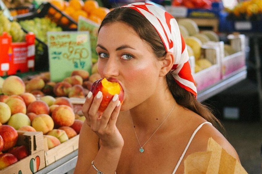 Une personne tenant une pomme dans une épicerie, avec divers fruits et légumes en arrière-plan. 4