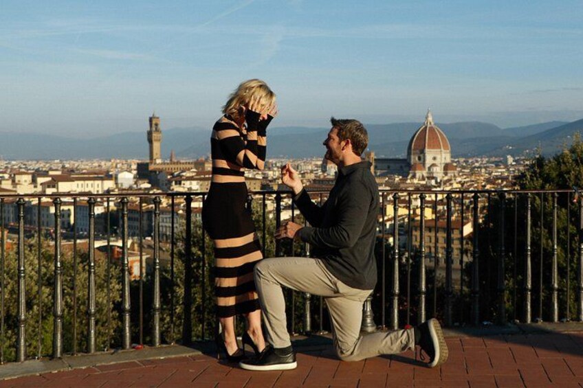 Un couple se tient sur un balcon donnant sur une vue panoramique de la ville, avec un dôme et une tour imposants en arrière-plan. 5