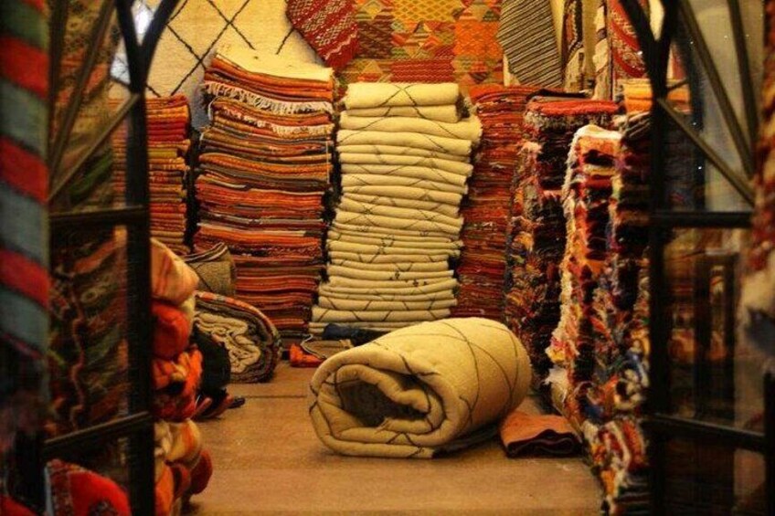 Un mercado con pilas de textiles coloridos y una manta grande enrollada en el centro. 4