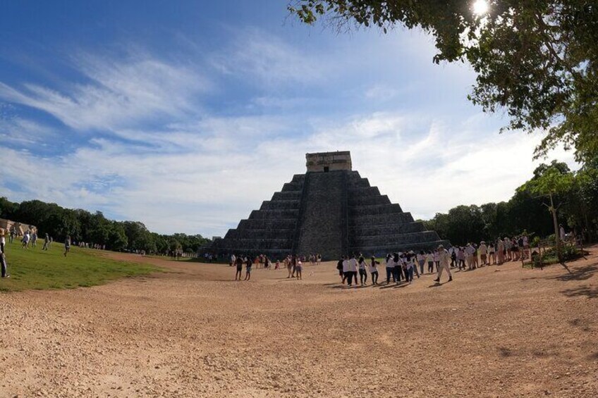 A large pyramid structure surrounded by a grassy area with people walking around. 1
