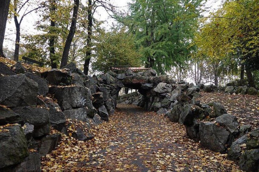 A stone bridge over a rocky path with autumn leaves scattered on the ground. 2