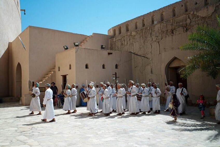 A group of people in white robes standing in a courtyard with a building in the background. 1