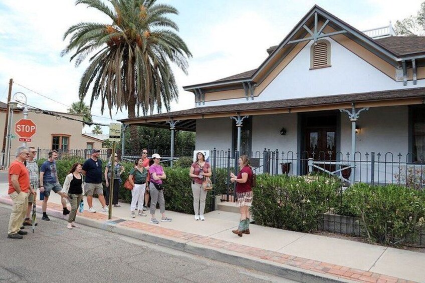 A group of people standing on a sidewalk in front of a building with a palm tree and a stop sign. 2