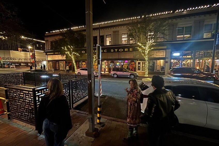 A nighttime street scene with illuminated storefronts, a pedestrian crossing, and a parked car. 5